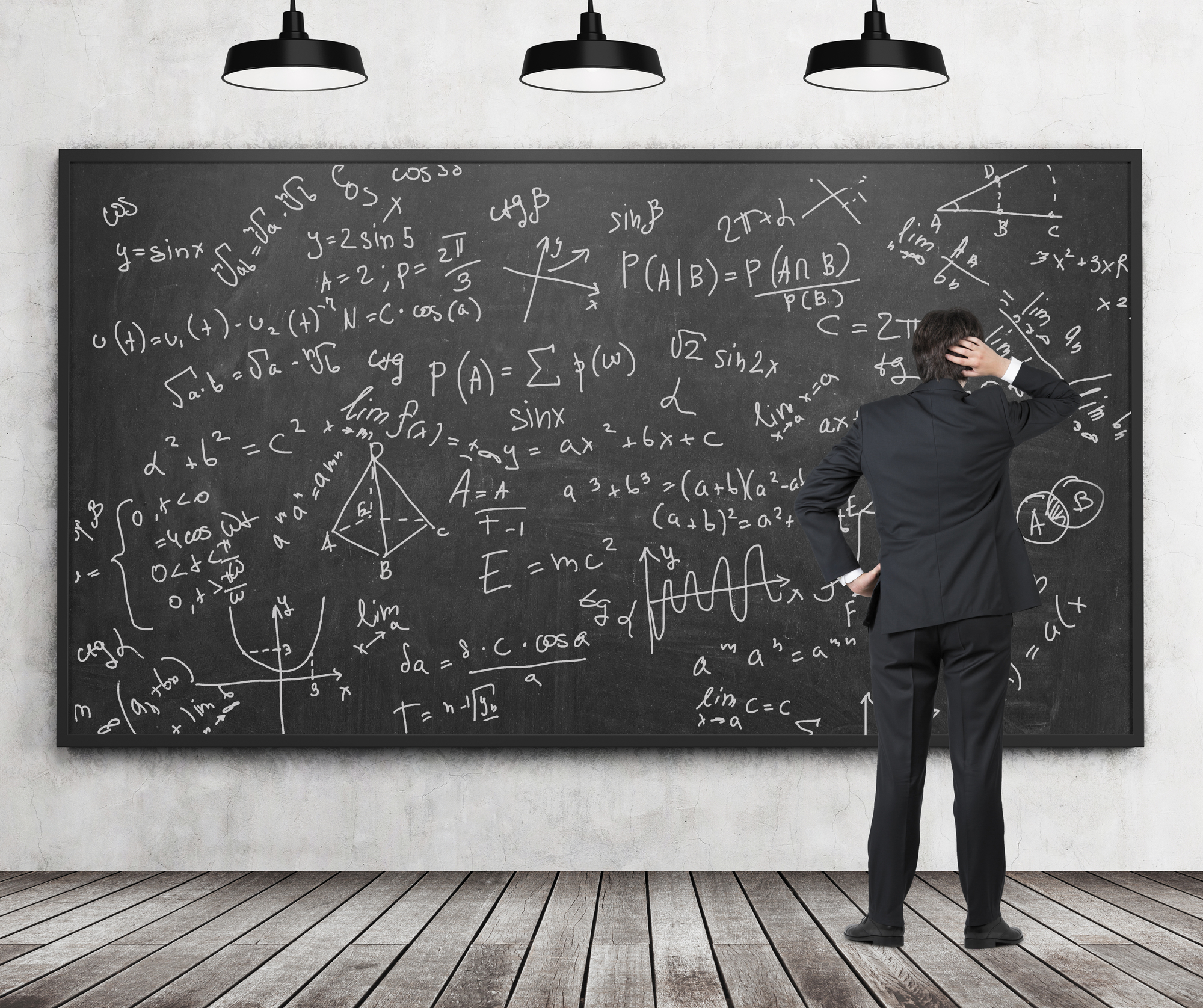 Rear view of man in suit staring at blackboard with formulas in confusion. Classroom with concrete wall and wooden floor. Concept of studying and exact sciences.